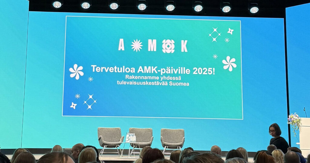 [Alt-teksti; AMK-päivien yleisöä katsomassa suurnäyttöä, jossa lukee Tervetuloa AMK-päiville.]