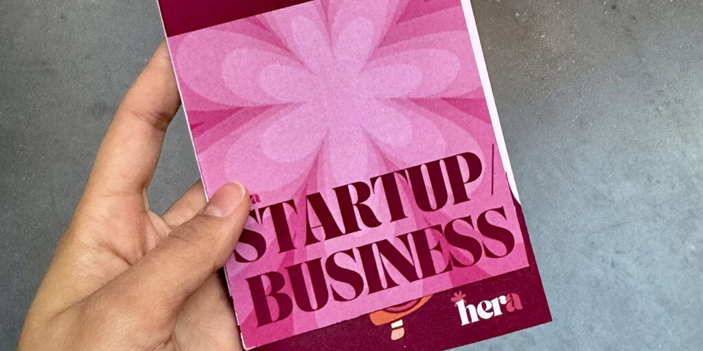 [Alt text: a hand helding a pink booklet with title startup business.]