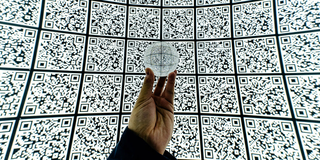 henkilö pitelee kädessään kirkasta lasipalloa QR-koodi taustan edessä