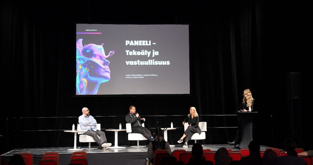 [Alt-teksti: paneelikeskustelussa esiintymislavalla neljä henkilöä.]