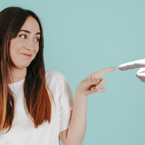A person smiling and touching the finger of an artificial robot hand.