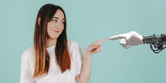 A person smiling and touching the finger of an artificial robot hand.
