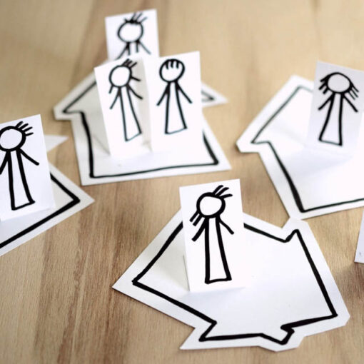 [Alt. Teksti: Paperista leikattuja piirroshahmoja ihmisistä, jotka ovat asetettu paperille piirrettyjen talojen päälle.]