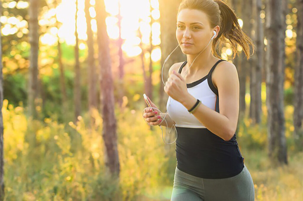 A female runner in sportswear jogging along a forest trail surrounded by green trees