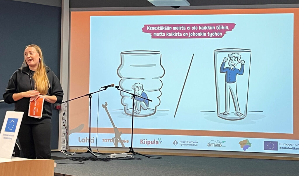 [Alt-teksti: henkilö pitää presentaatiota, kuvan yllä teksti kenestäkään meistä ei ole kaikkiin töihin, mutta kaikista on johonkin työhön.]