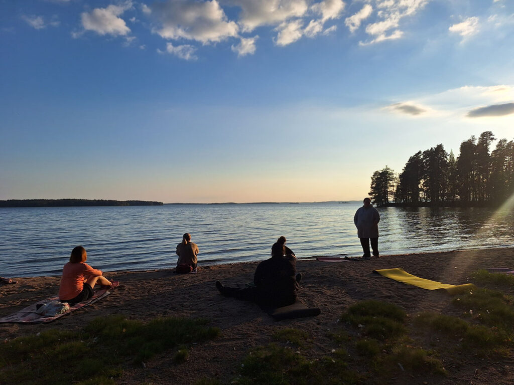 Ihmisiä istumassa rannalla iltahämärässä.