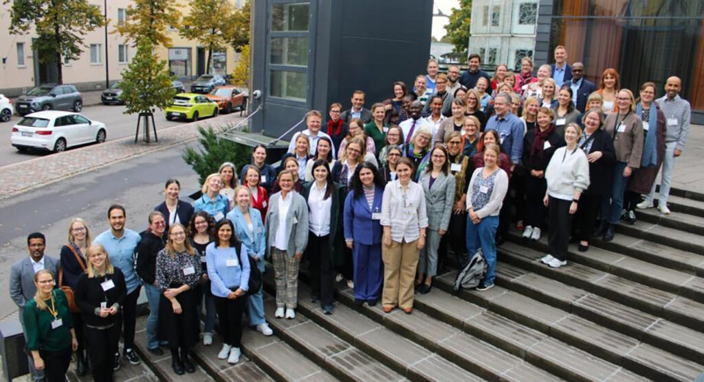 [Alt text: a large group of smiling people standing at the stairs outside of a huge building.]
