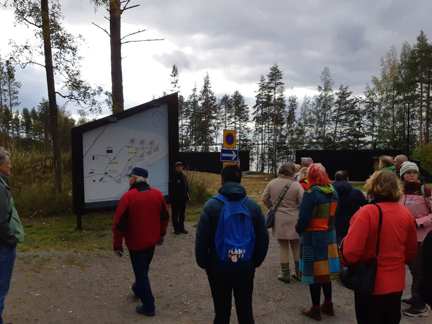 [Alt-teksti: ihmisiä ulkona opastekartan edessä. Taustalla järvi ja mäntymetsä.]