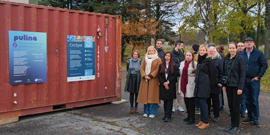 Vasemmalla vanha merikontti, jonka kyljessä Pulina- ja CircSyst-hankkeiden julisteet. Oikealla ryhmä ihmisiä.