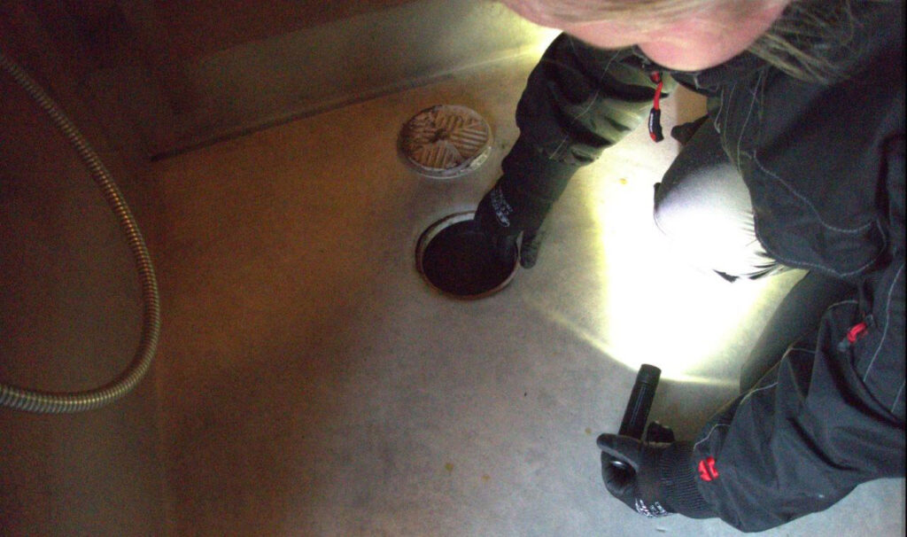 [Alt-teksti: henkilö tutkimassa betonilattialla olevaa lattiakaivoa ja sen ympäristöä.]