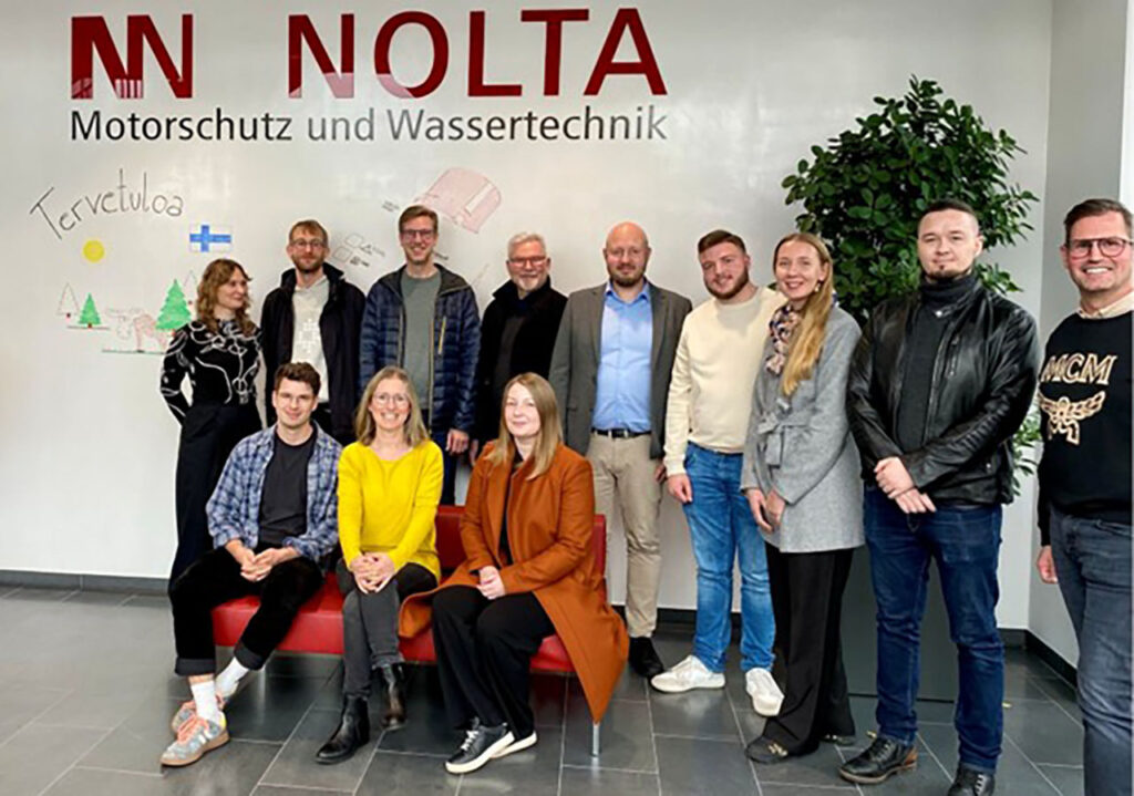 [Alt-teksti: ryhmä ihmisiä aulatilassa, jossa on sohva ja viherkasvi.]