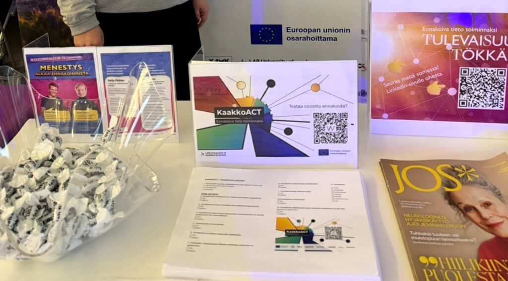 [Alt-teksti: pöytä, jossa on tarjolla tiedotusmateriaalia ja suuressa kulhossa paperipäällysteisiä karamelleja.]