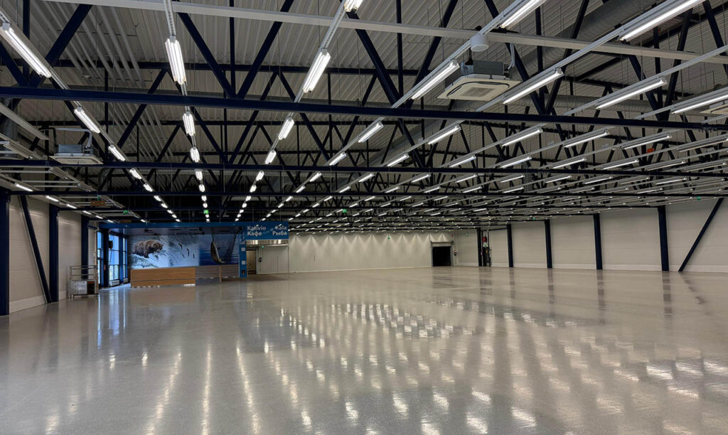 [Alt-teksti: avara ja matala, kirkkaasti valaistu ja vielä tyhjillään oleva teollisuushallitila.]