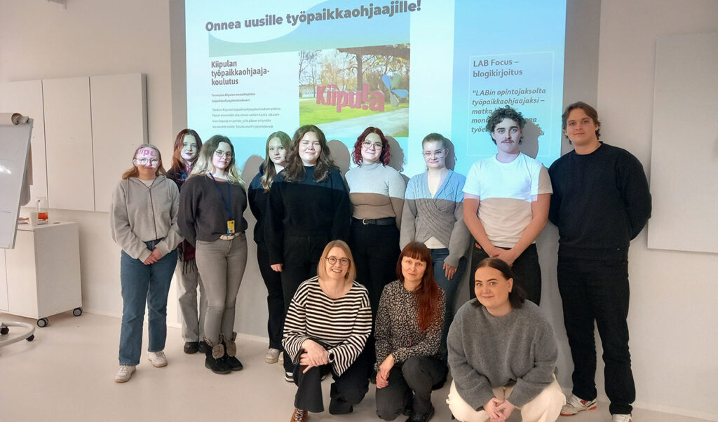 [Alt-teksti: ryhmä ihmisiä, takana näkyy heijastettuna esitys, jossa lukee onnea uusille työpaikkaohjaajille.]