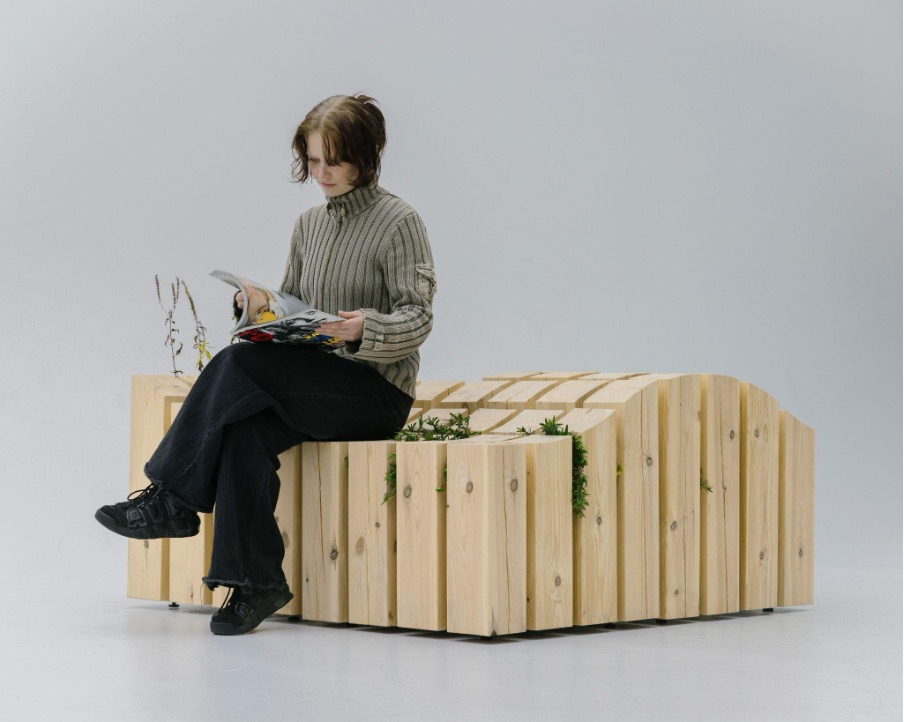 Ihminen lukee lehteä ja istuu kasvillisuuskalusteista muodostetulla penkillä.
