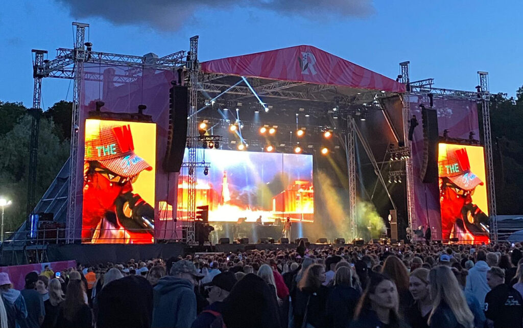 [Alt-teksti: suuren ulkoilmalavan edessä on satapäinen yleisö, lavan kahta puolta on kookkaat näytöt, joissa näkyy esiintyjä.]