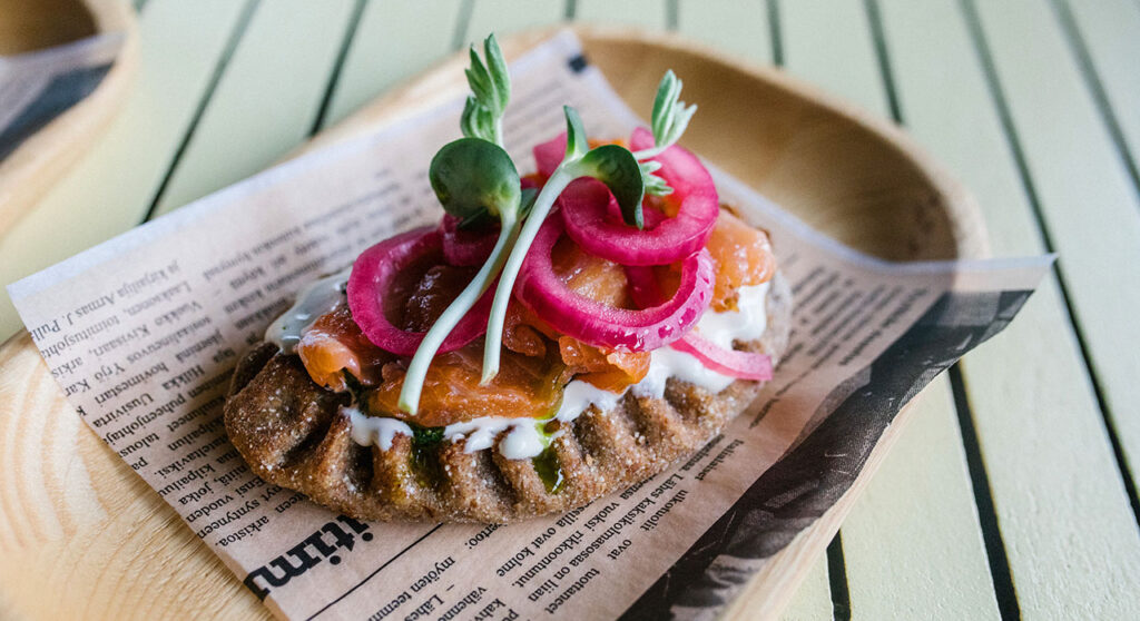 [Alt-teksti: puisella tarjoilualustalla oleva karjalanpiirakka, joka on höystetty monenlaisilla päällyksillä.]