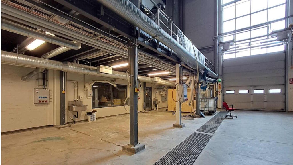 Korkea betonilattiainen halli, jossa kulkee putkistoja.