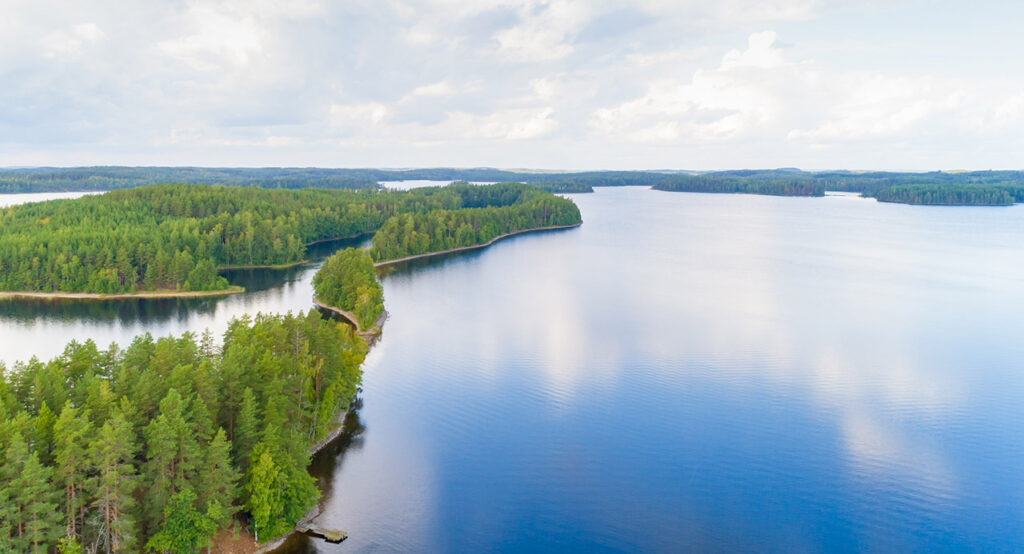 [Alt-teksti: laajalle avautuva kesäinen järvimaisema, jota halkovat metsäiset kannakset ja saaret.]