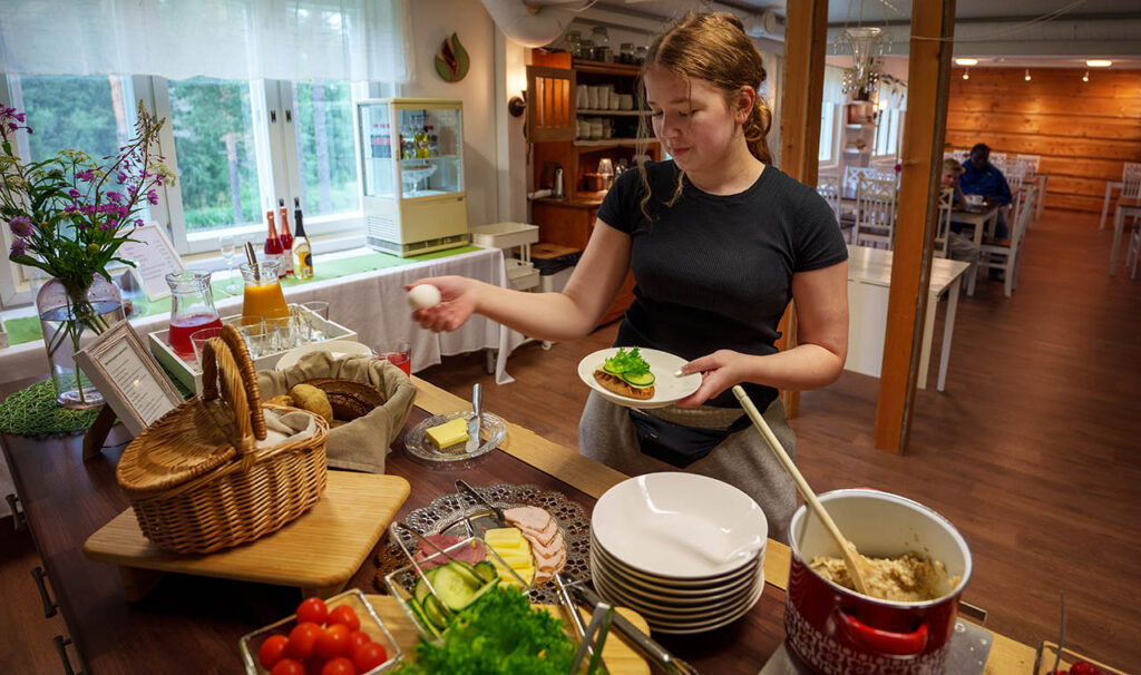 [Alt-teksti: maalaismaisessa suuressa pirtissä oleva runsas noutopöytä, jonka äärellä on henkilö keräilemässä lautaselleen syötävää.]