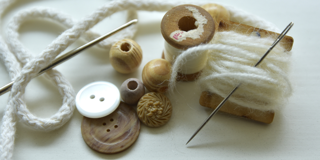 Ompelutarvikkeita: villalankaa, neulaa, nappeja ja nauhaa.