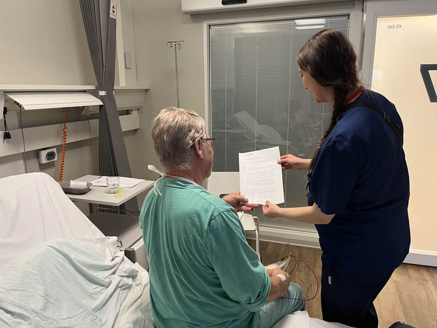 [Alt-teksti: hoitaja lukee ohjeita sängyllä istuvalle potilaalle.]