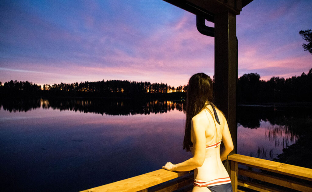 [Alt-teksti: iltakuva järven rannalle rakennetulta saunaterassilta, kesäinen auringonlasku horisontissa.]