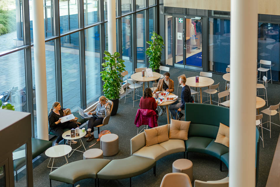 [Alt-teksti: huone, jossa on pöytiä, tuoleja ja sohvaryhmä. Ihmisiä työskentelee tietokoneiden kanssa.]