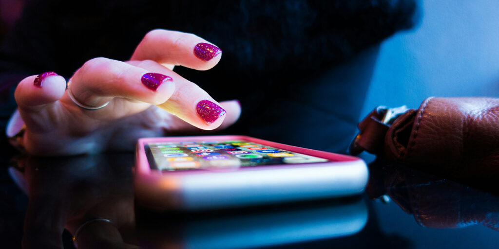 Lähikuva kädestä, joka käyttää älypuhelinta tasaisella pinnalla; kosketusnäytön käyttö kuvaa arkista digipalvelun käyttötilannetta.