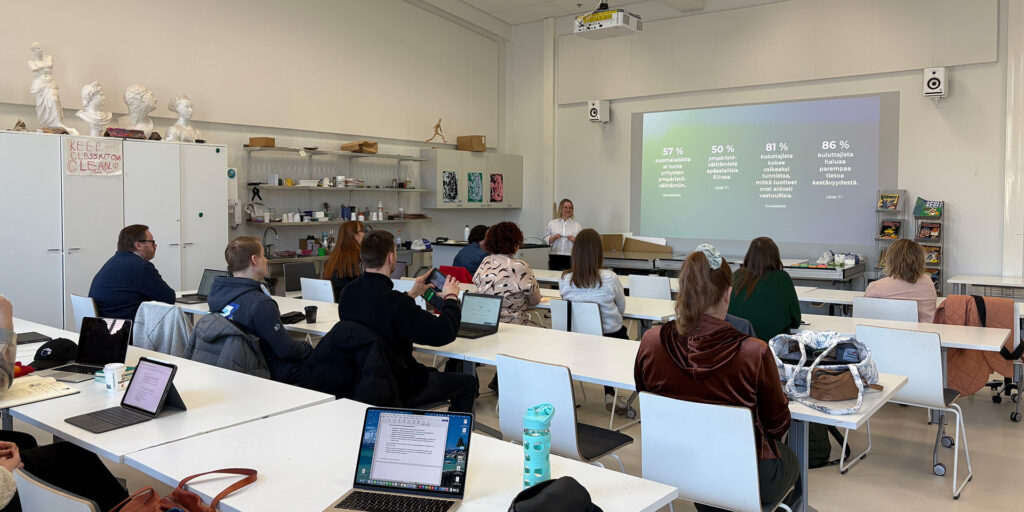 Luokkatila, jossa opiskelijoita. Kouluttaja edessä luennoimassa, videotykillä seinälle heijastettu opetusmateriaali.