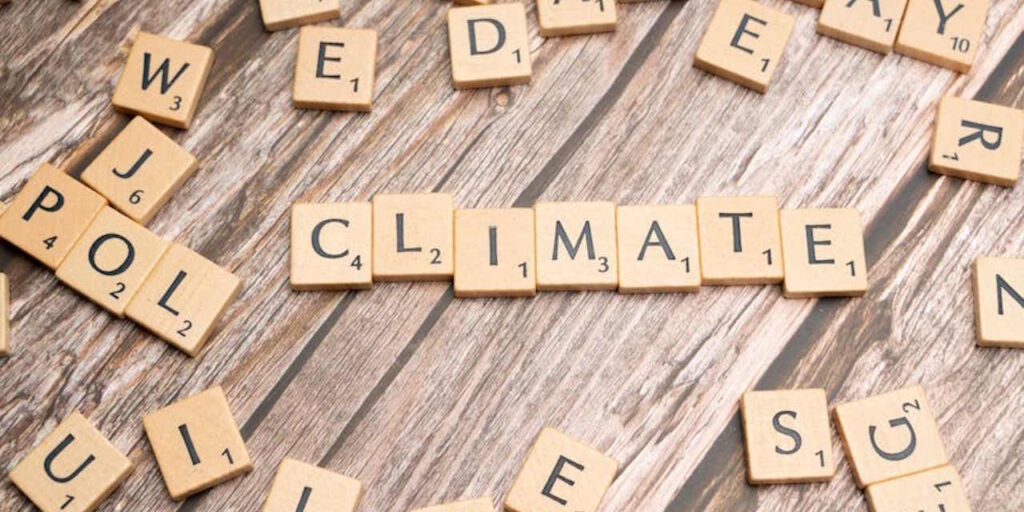 Scrabble tiles spelling the word “climate” on a wooden table, surrounded by other letters.