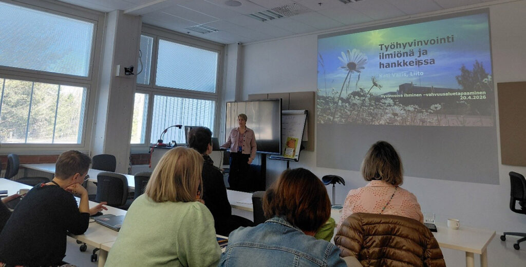 [Alt-teksti: henkilö pitää esitystä luokkamaisessa suuressa tilassa.]