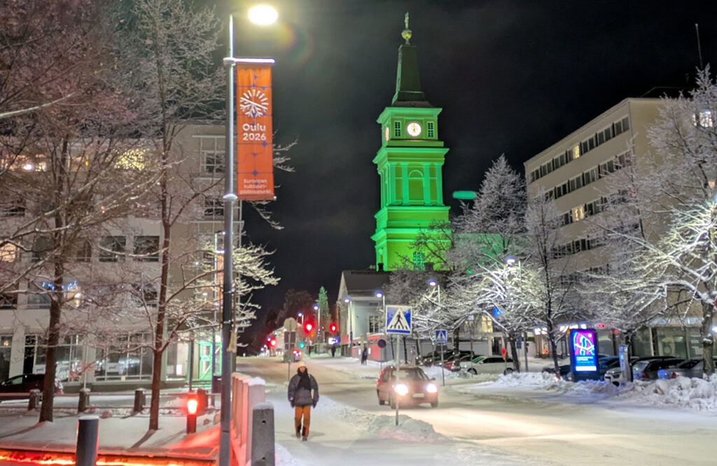 [Alt-teksti: talvinen katumaisema, jossa valaistut rakennukset ja valopylväät valaisevat pimeyttä.]