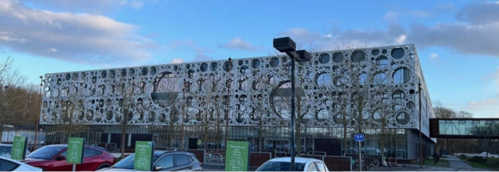 [Alt-teksi: harmaa neliönmuotoinen yliopistorakennus, jonka etuseinässä on pallomaisia kuviointeja.]