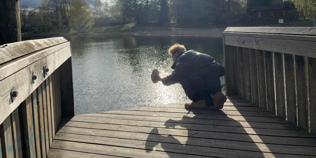 A person at the end of a pier, measuring water visibility with a Secchi desk.