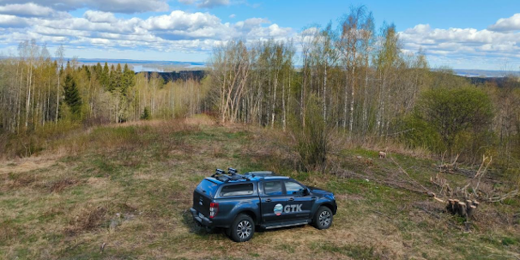 Etualalla musta maastoajoneuvo, taustalla metsää.