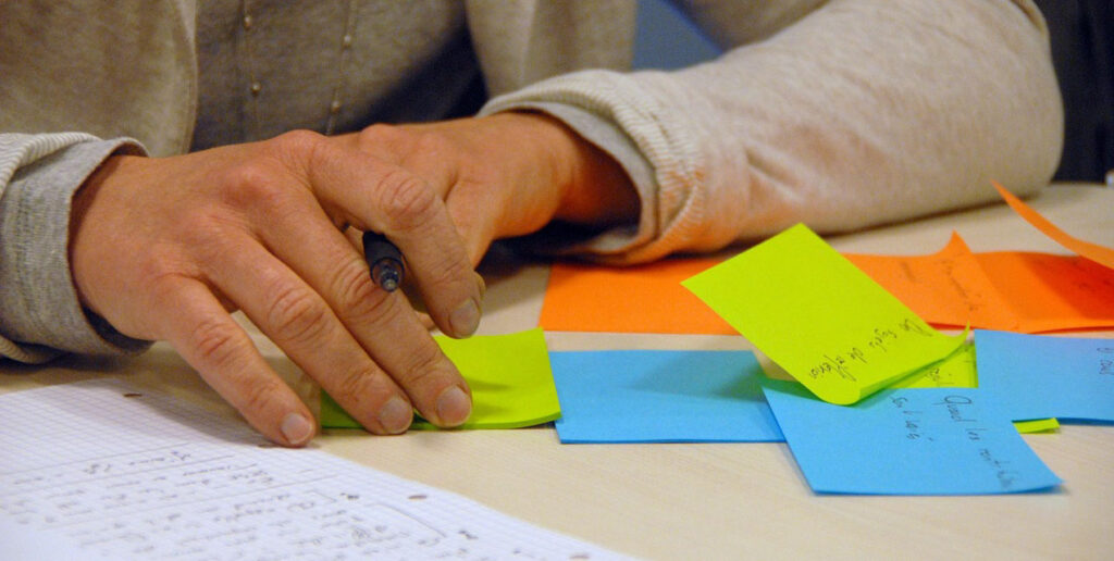 Erivärisiä post it -lappuja pöydällä, joihin työpajaan osallistuva kirjoittaa. 