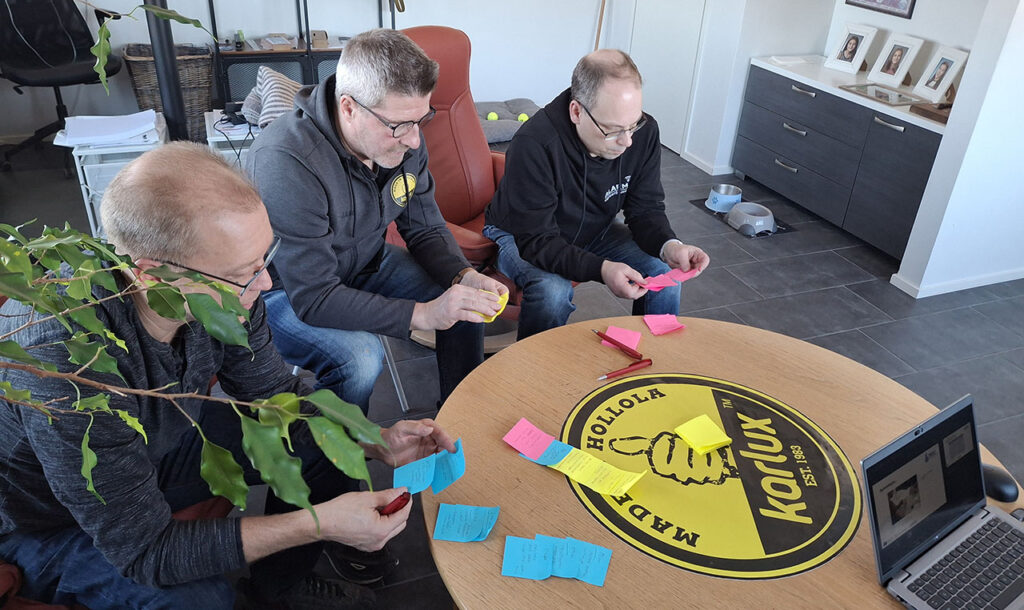 [Alt-teksti: kolme henkilöä pöydän ääressä käsissään post it -lappuja, joihin on kirjoitettu tekstiä.]