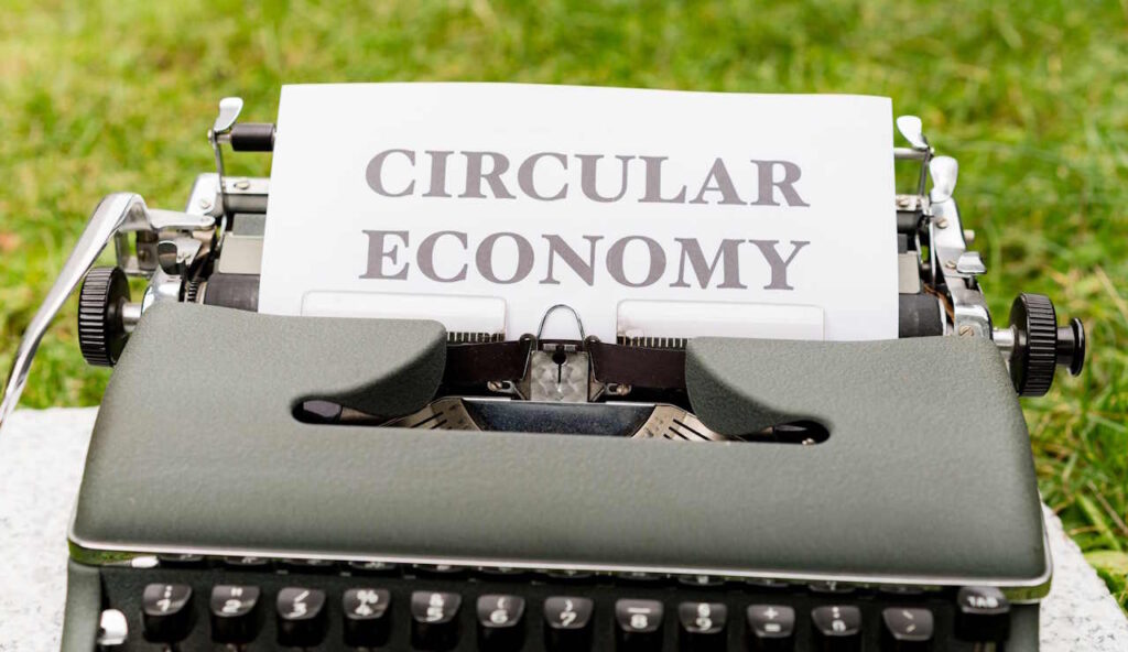Kirjoituskone, jossa on paperi tekstillä Circular Economy. Taustalla vihreä ruohikko.
