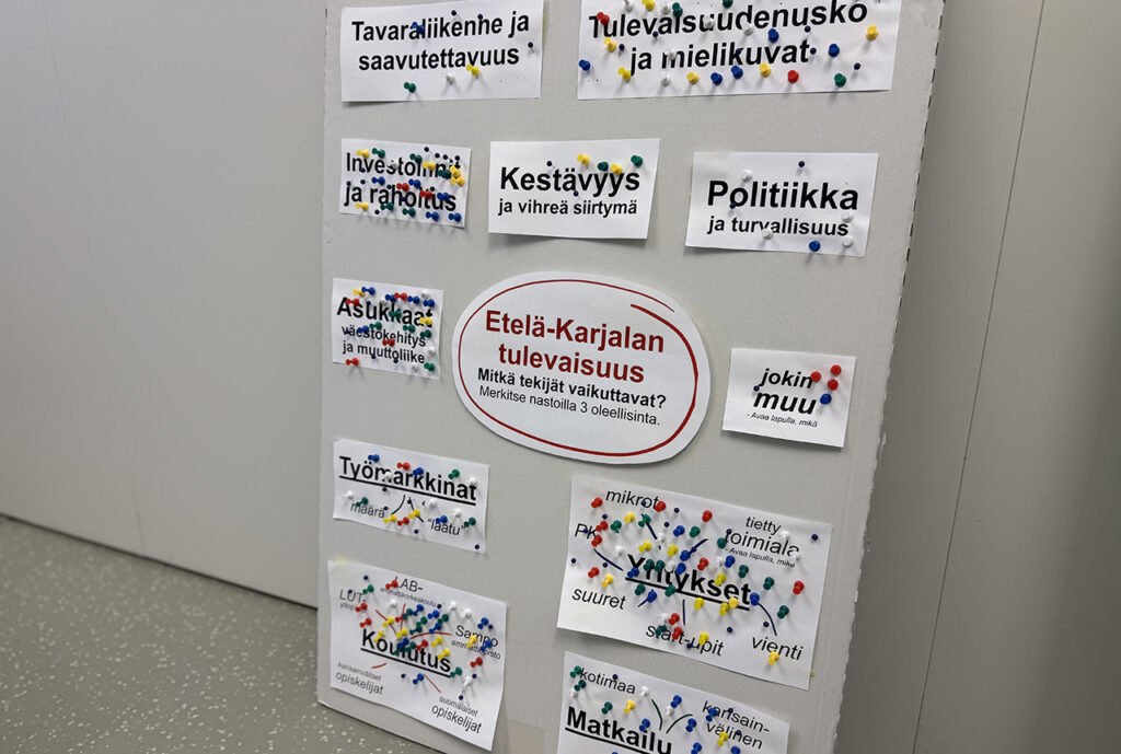 [Alt-teksti: suurelle taululle on kiinnitetty lappuja, joissa lukee esimerkiksi asukkaat, työmarkkinat, matkailu ja koulutus, lapuissa on kymmenittäin erivärisiä neulanpäitä.]