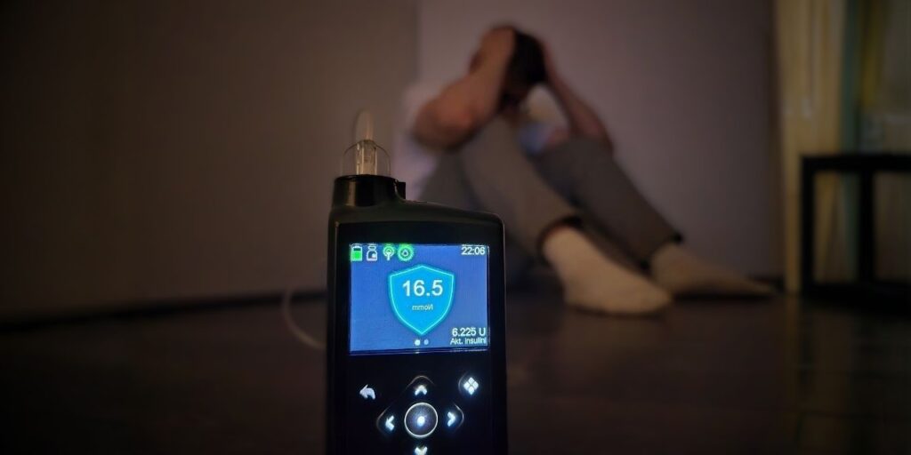 Insuliinipumppu näyttää korkeaa verensokeriarvoa. Taustalla diabetesta sairastava henkilö pitelee päätään.