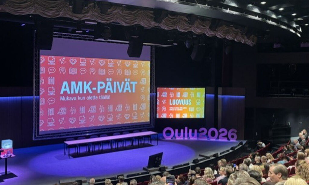 Teatterin tyhjä näyttämö. Yleisöä katsomossa. Screenillä lukee AMK-PÄIVÄT, mukava kun olette täällä!