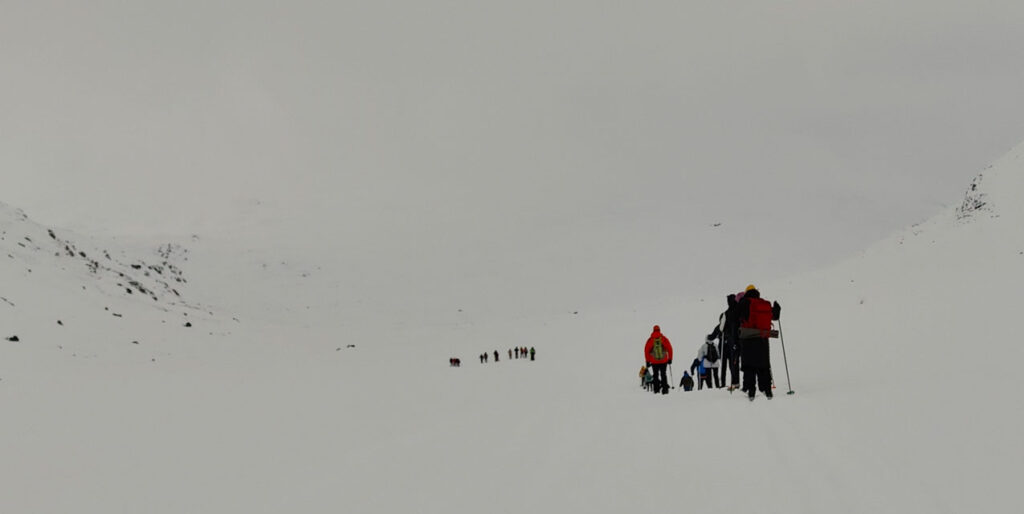 Skiers making their way through a fell landscape surrounded by snow under a partly cloudy sky.