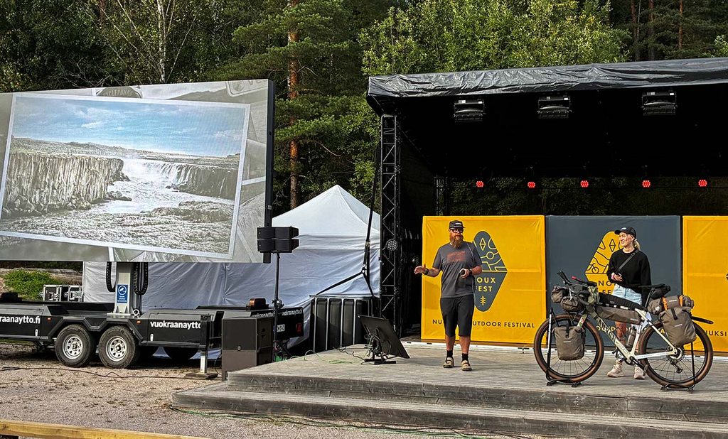 [Alt-teksti: messulava, jolla seisova mies pitää esitystä ja hänen vieressään suurella heijastustaululla on näkymiä jylhästä vesiputouksesta.]